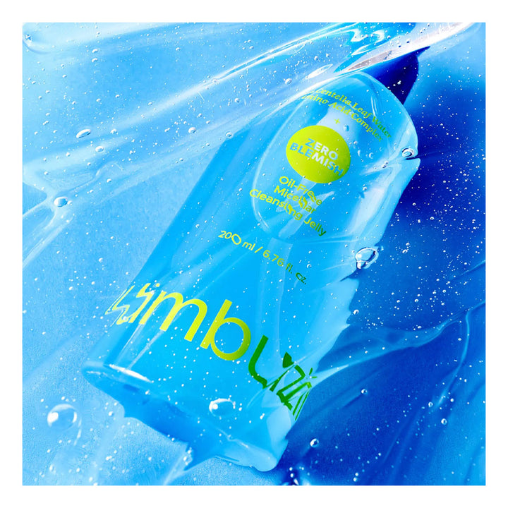 A clear blue bottle of Wimbli Zero Alcohol free mouthwash with yellow lettering, shown diagonally amidst water droplets and liquid swirls on a white background.