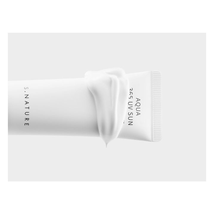 A white cosmetic tube with a thick swirl of white cream draped over the center, shown on a light gray background. The tube has black vertical text reading &