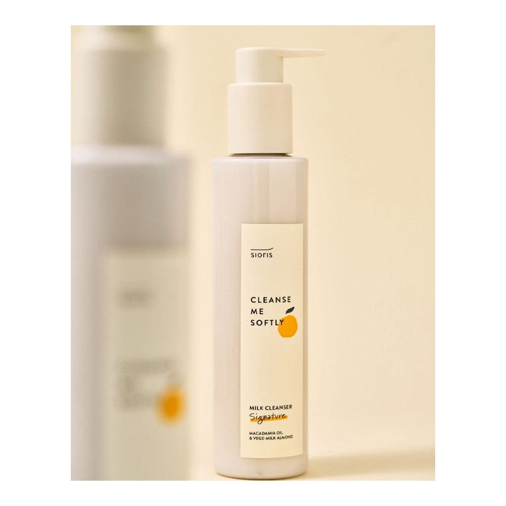 A bottle of Sions Cleanse Me Softly Milk Cleanser with a white pump dispenser and cream-colored label, set against a soft beige background with a blurred second bottle in the background.