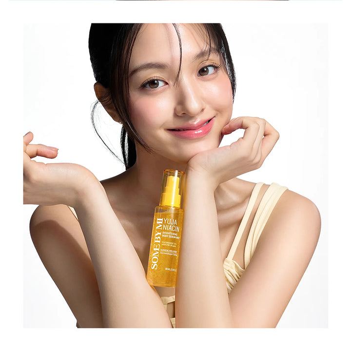 A woman with dark hair pulled back holds a bottle of Some By Mi Vega Lucena hair oil against a clean white background.