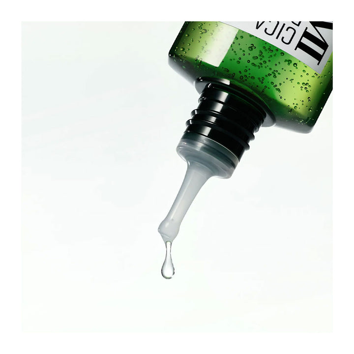 A close-up of a green glittery cosmetic dropper bottle with a clear silicone pipette tip dispensing a drop of clear gel or serum against a white background.