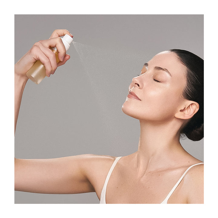 Woman applying a facial mist spray to her face against a neutral background