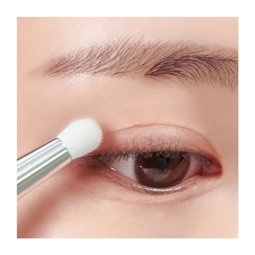 Close-up of a person's eye with an eyebrow and eyelid, while a makeup brush applies product near the eye area.