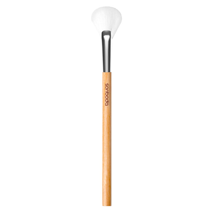 A single makeup brush with a light natural wood handle, a black ferrule, and white bristles, shown vertically against a plain white background. The brand name &