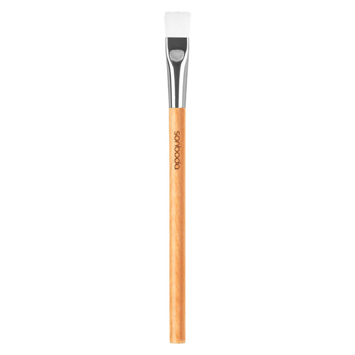 A flat-tip makeup brush with a light natural wood handle, a silver ferrule, and white bristles, shown vertically on a plain white background. The brand name &