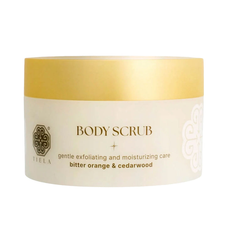 A white and gold jar of TIELA Body Scrub, specifically the bitter orange &amp; cedarwood variant, shown on a clean white background.