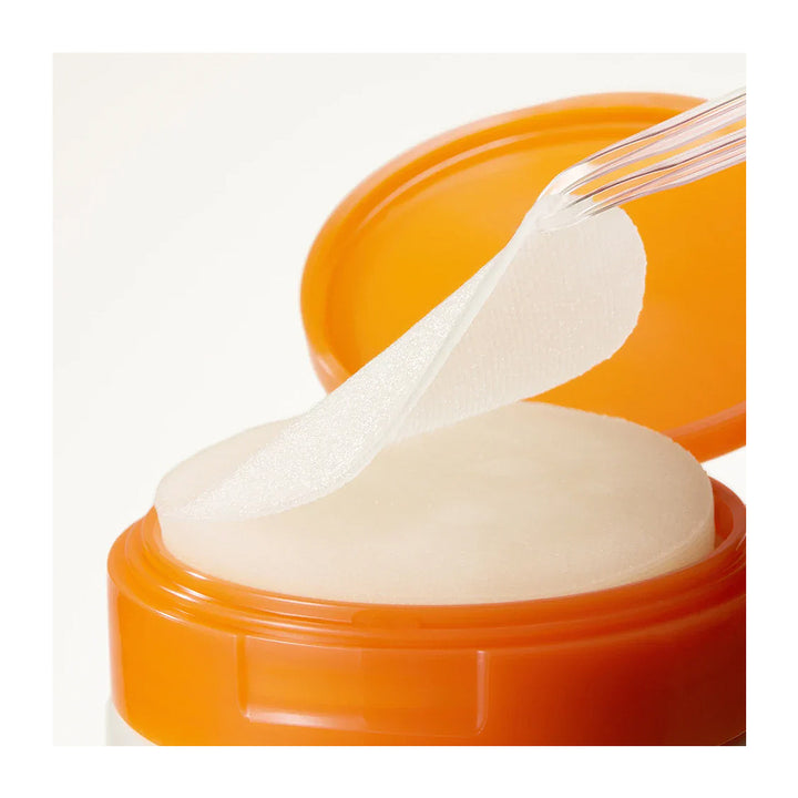 An open jar of eye cream with a translucent white patch applied to the eye area, shown against a clean white background.