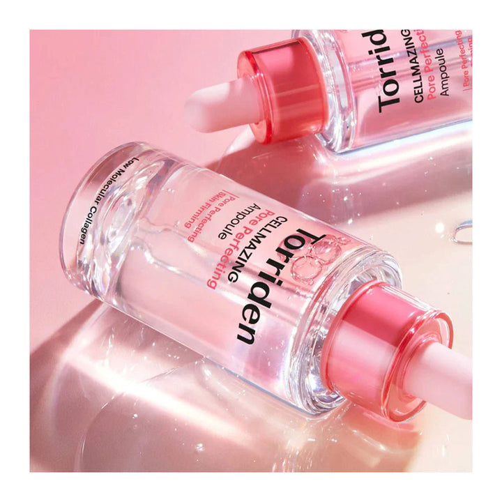 Two clear cosmetic dropper bottles with pink caps and pink liquid inside, labeled Torriden Cell-Maximizing Ampoule, arranged on a glossy pink reflective surface.