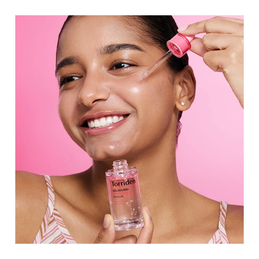 A woman with glowing skin applies a pink-toned skincare serum using a dropper from a clear bottle labeled Torriden Gel-Niacin, set against a solid pink background.