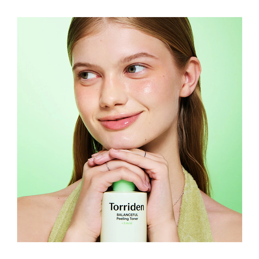 A woman with light brown hair holds a bottle of Torriden Balanceful Picking Toner against a light green background.