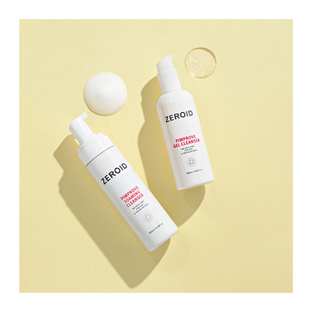 Two white pump bottles of ZEROID facial cleansers, one foaming cleanser and one gel cleanser, arranged diagonally on a pale yellow background with a white sphere and a clear gel droplet prop.